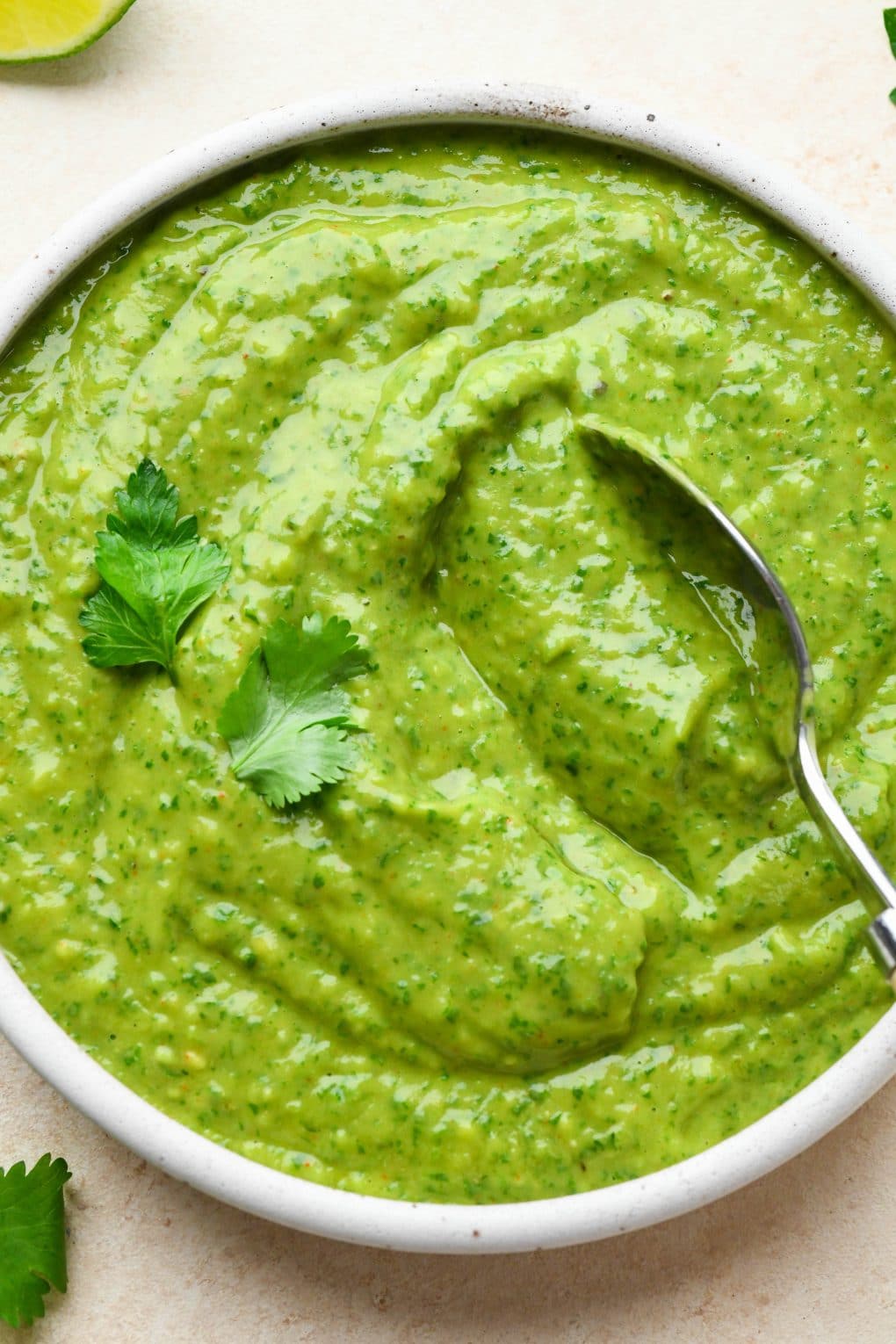 A spoon dipping into a small bowl of bright green avocado herb green sauce.