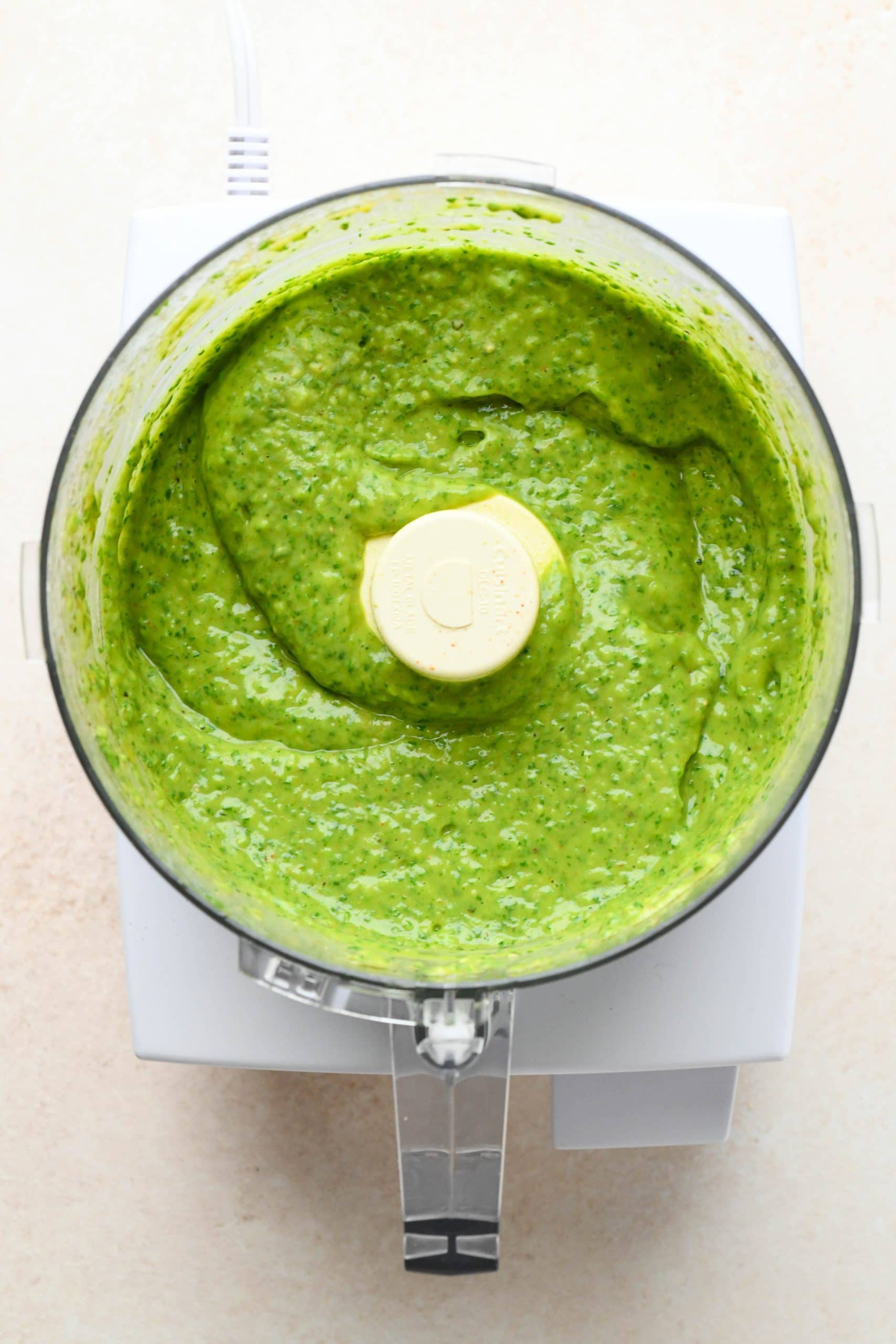 How to make avocado herb green sauce: Sauce processed together in the bowl of a food processor.