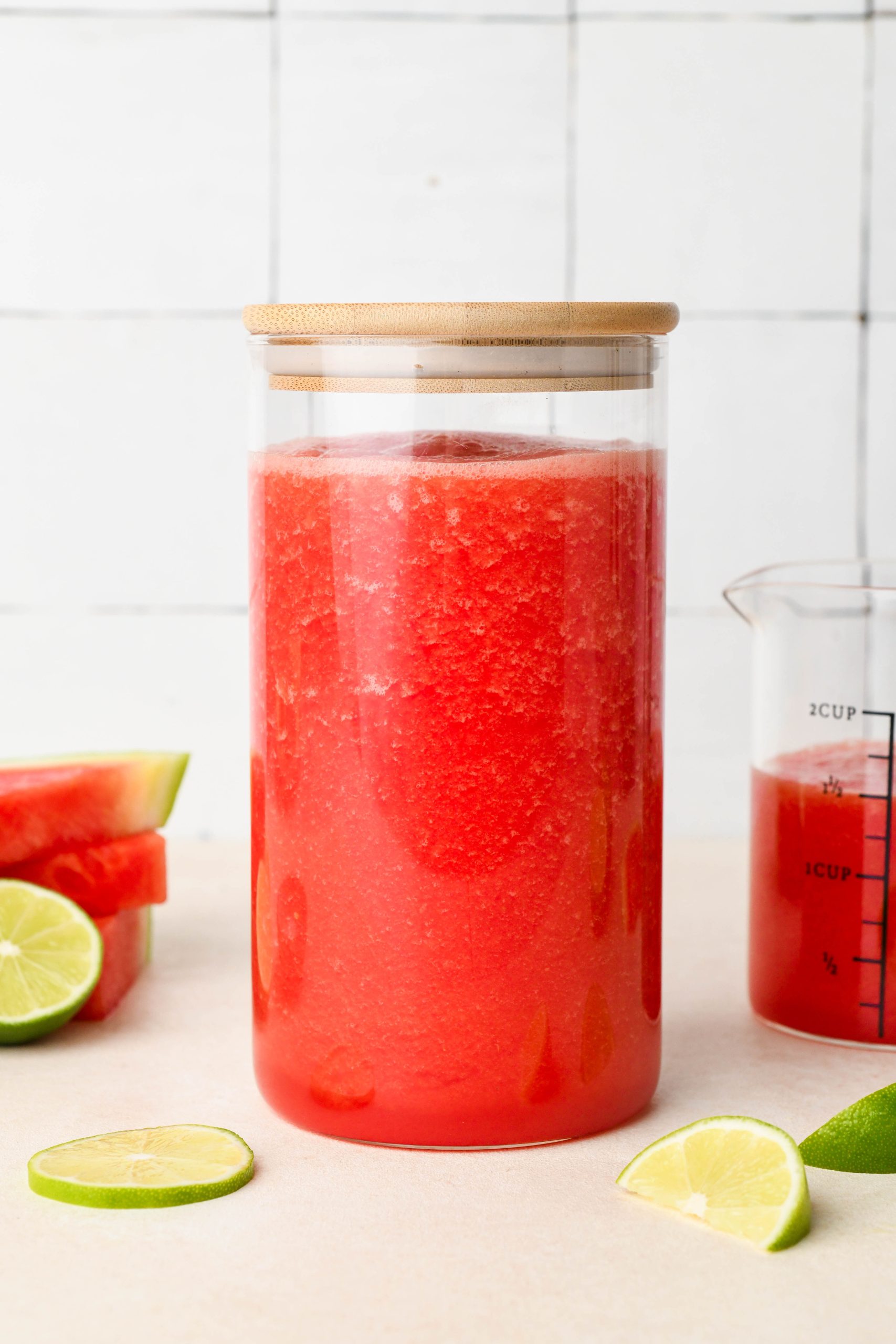 A large glass jar with a wooden lid filled with bright pink watermelon juice.