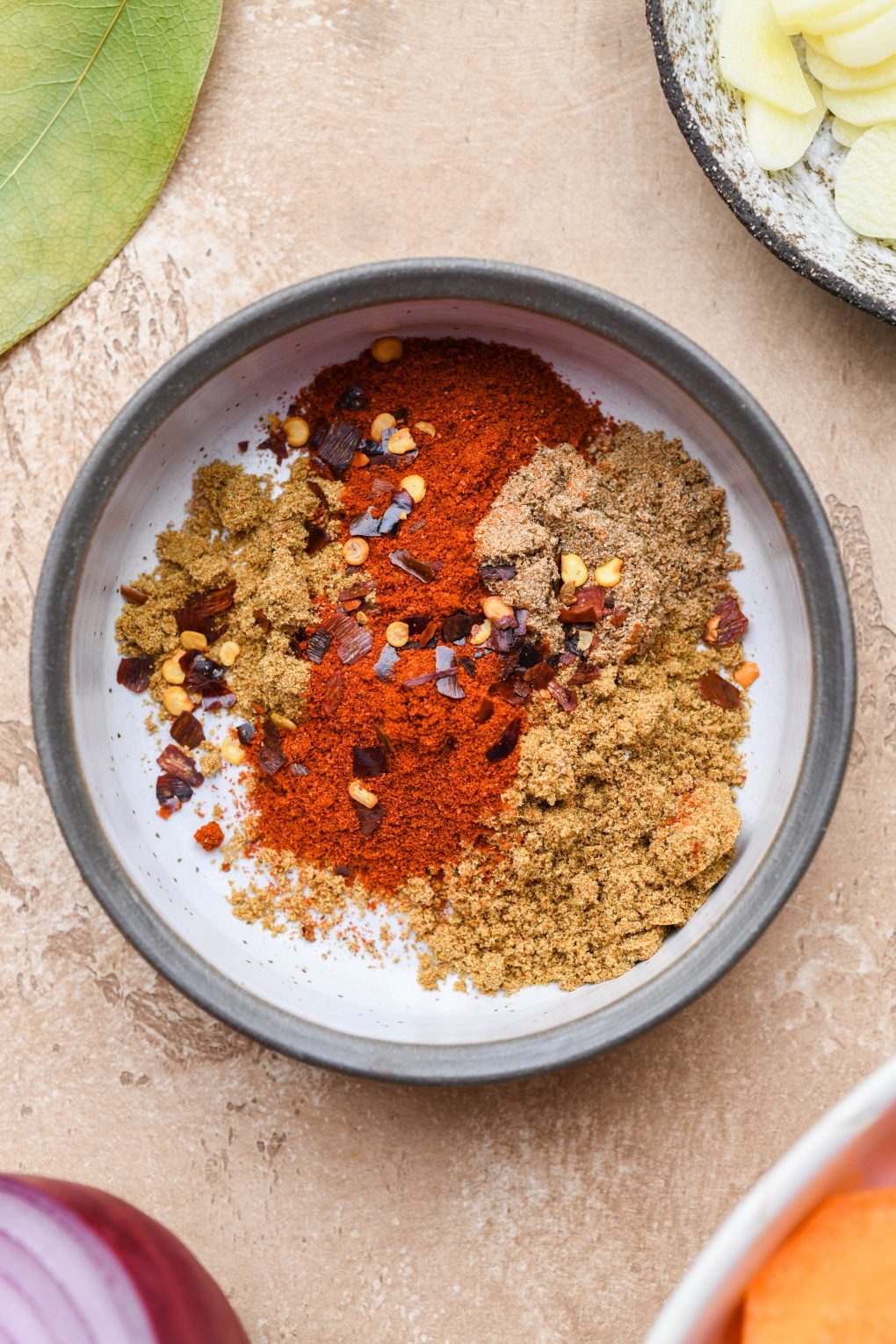 Close up image of a small dish filled with spices for carrot soup - paprika, cumin, coriander, and chili flakes.