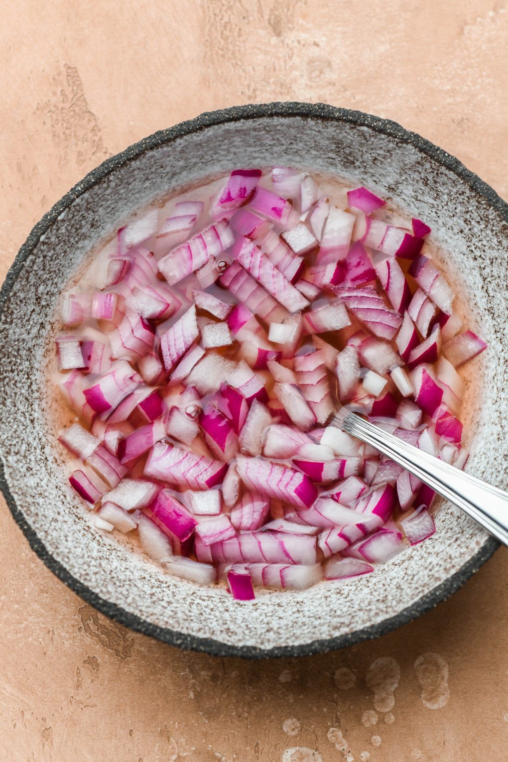 Chopped pickled red onions in a shallow textured bowl. On a light brown background.
