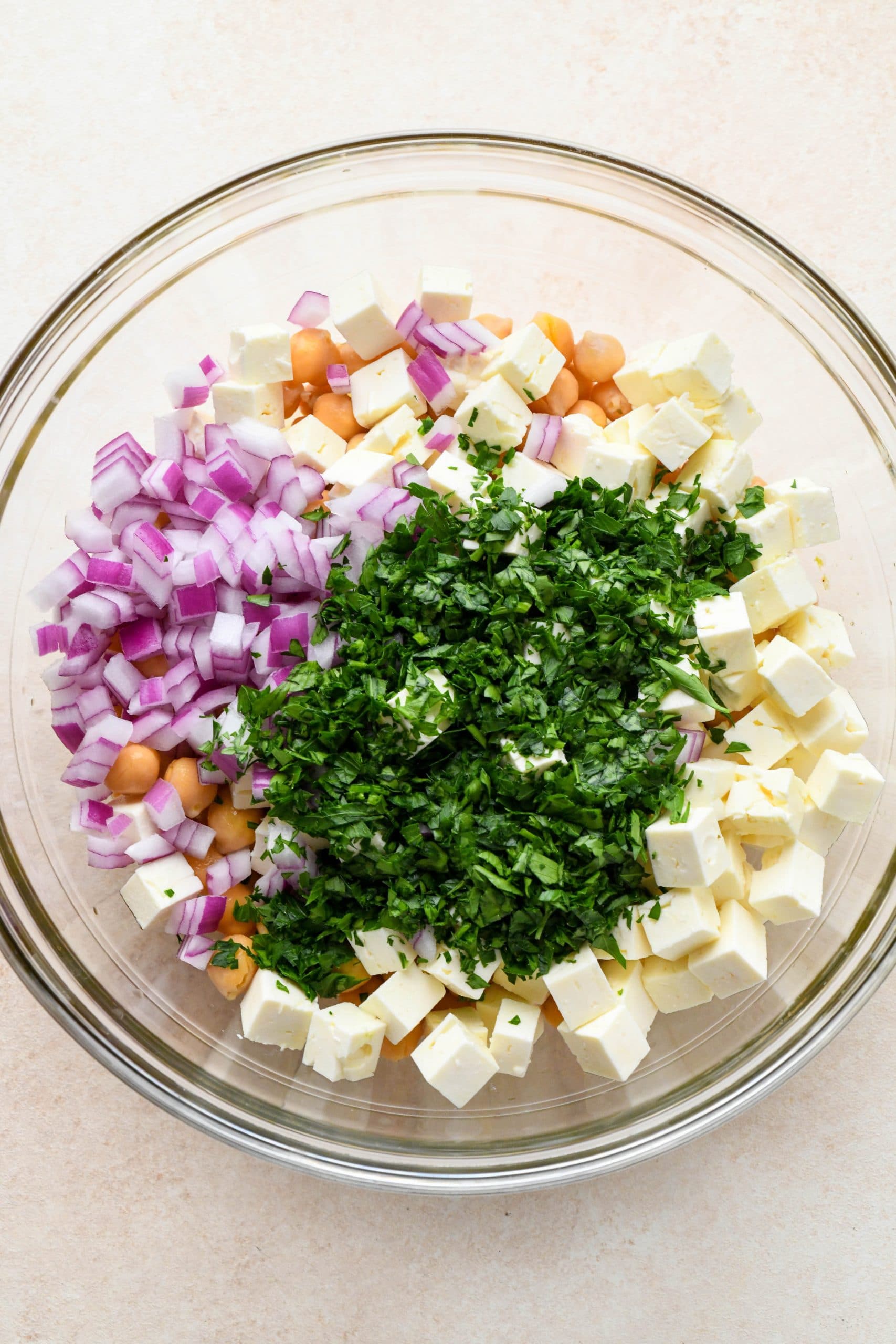 How to make lemony chickpea feta salad: Chickpeas, feta, herbs, and red onion added to the large glass bowl with dressing. 