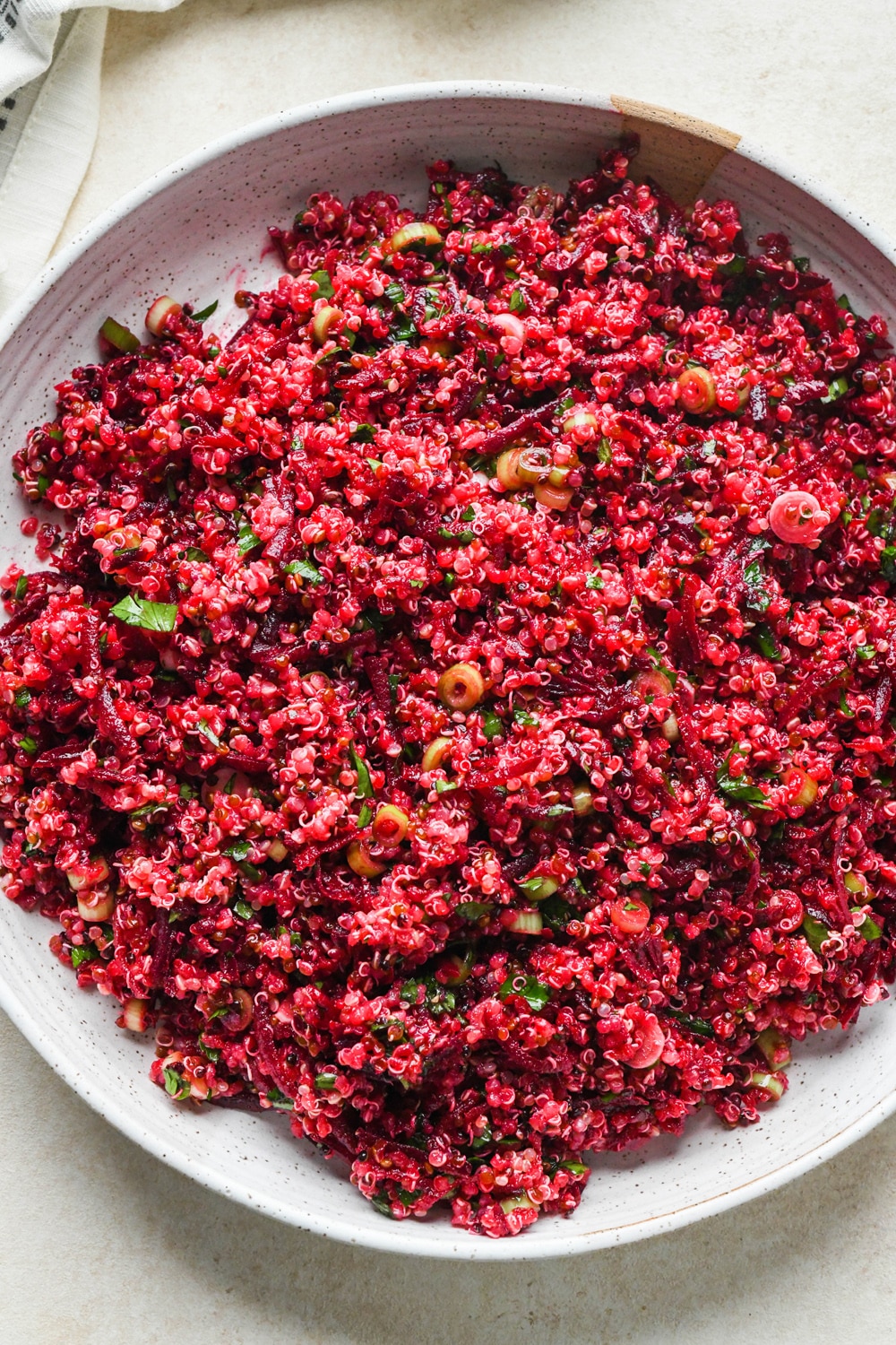 How to make quinoa and fresh beet salad: Deep pink quinoa salad in a large ceramic serving dish before garnishing with thinly sliced green onions, fresh parsley, and lemon wedges.