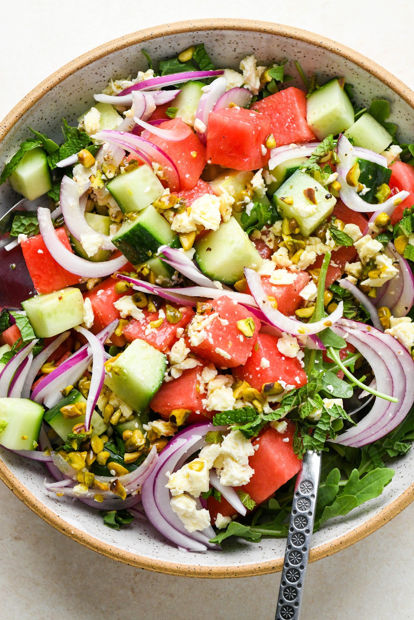 How to make watermelon arugula salad: Two large spoons tossing watermelon salad with dressing.