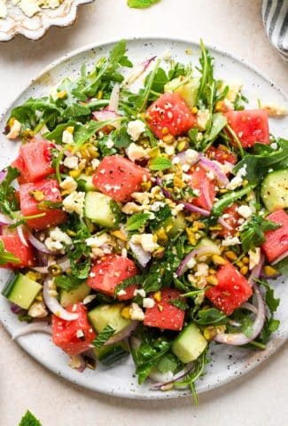 Watermelon and arugula salad with cucumber, feta, mint, and pistachios, piled high on a large white platter.