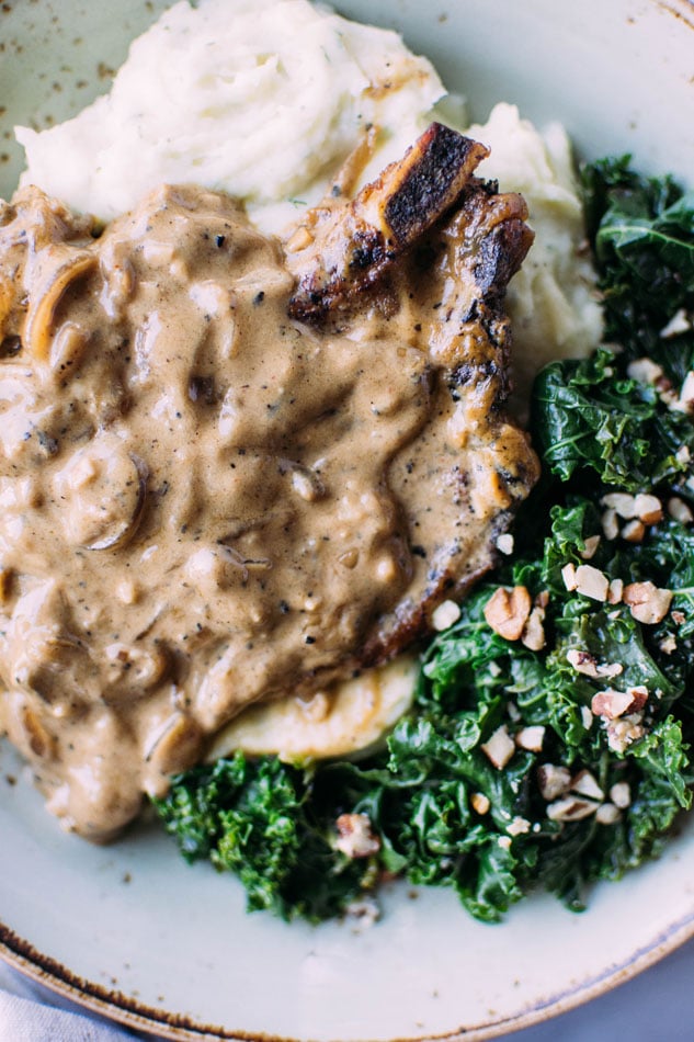Caramelized onion smothered pork chops with herb whipped parsnips and kale are here to take your gluten free // paleo dinner to the next level of comfort + satisfaction! Nestled in a creamy dairy free sauce these pork chops pair perfectly with dreamy whipped parsnips and bright and nourishing kale for the perfect comfort food meal.