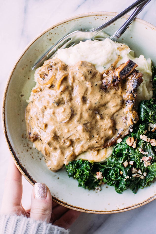 Caramelized onion smothered pork chops with herb whipped parsnips and kale are here to take your gluten free // paleo dinner to the next level of comfort + satisfaction! Nestled in a creamy dairy free sauce these pork chops pair perfectly with dreamy whipped parsnips and bright and nourishing kale for the perfect comfort food meal.