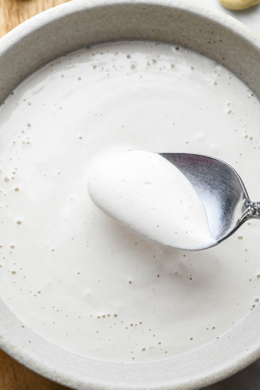 A spoon lifting out a bit of cashew cream made with 3/4 cup water to show the thinner consistency.