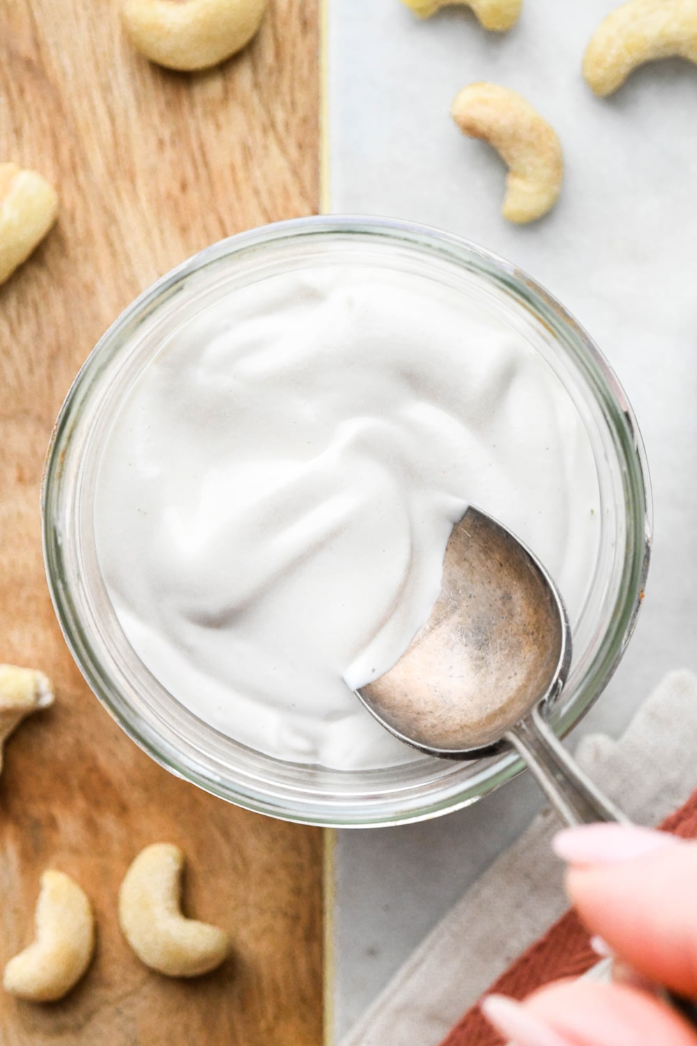 Blended cashew cream in a glass jar from the overhead perspective, with a spoon dipping into the jar to show the thick and creamy texture.