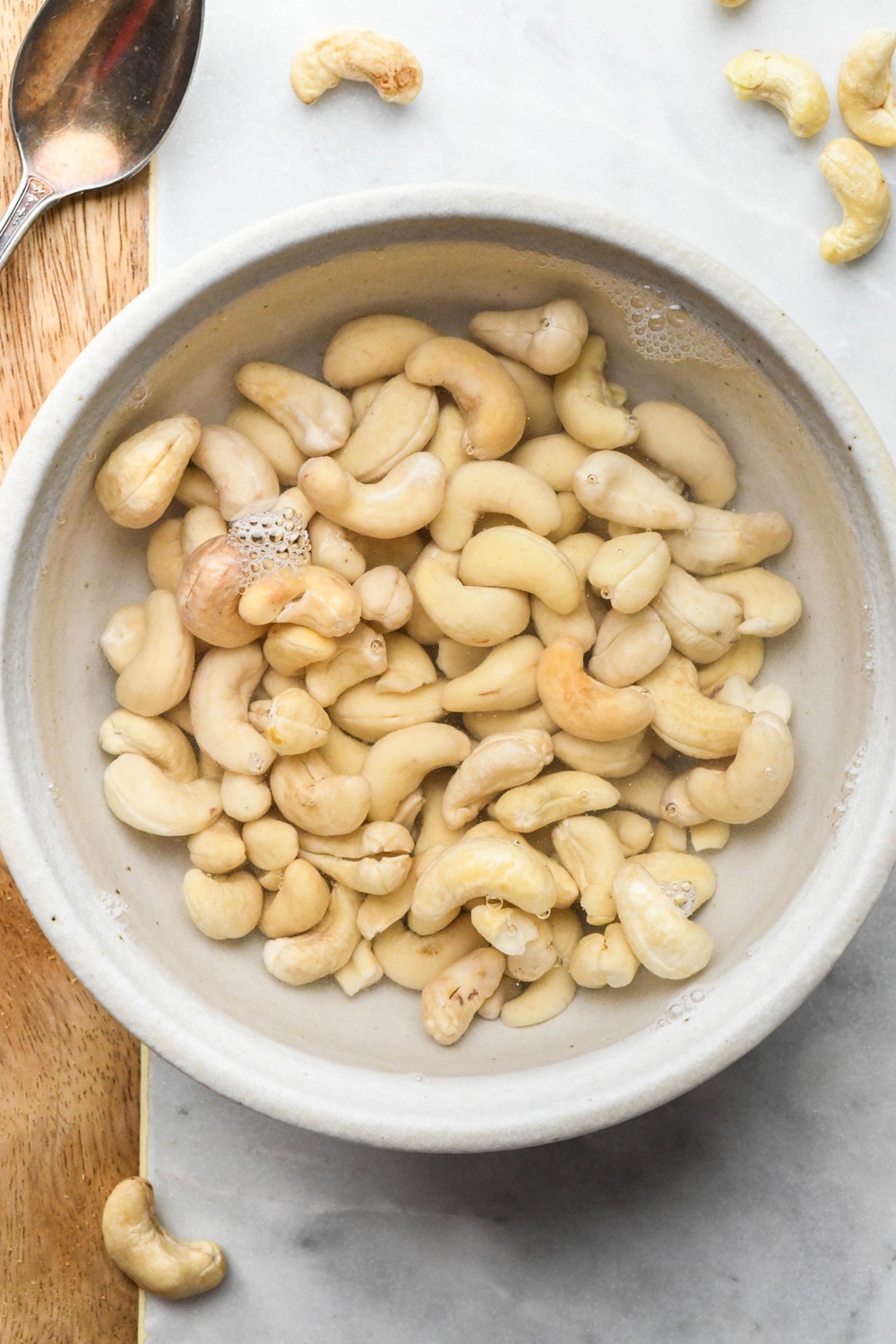 How to make cashew cream: Raw cashews in a ceramic bowl covered in hot water.