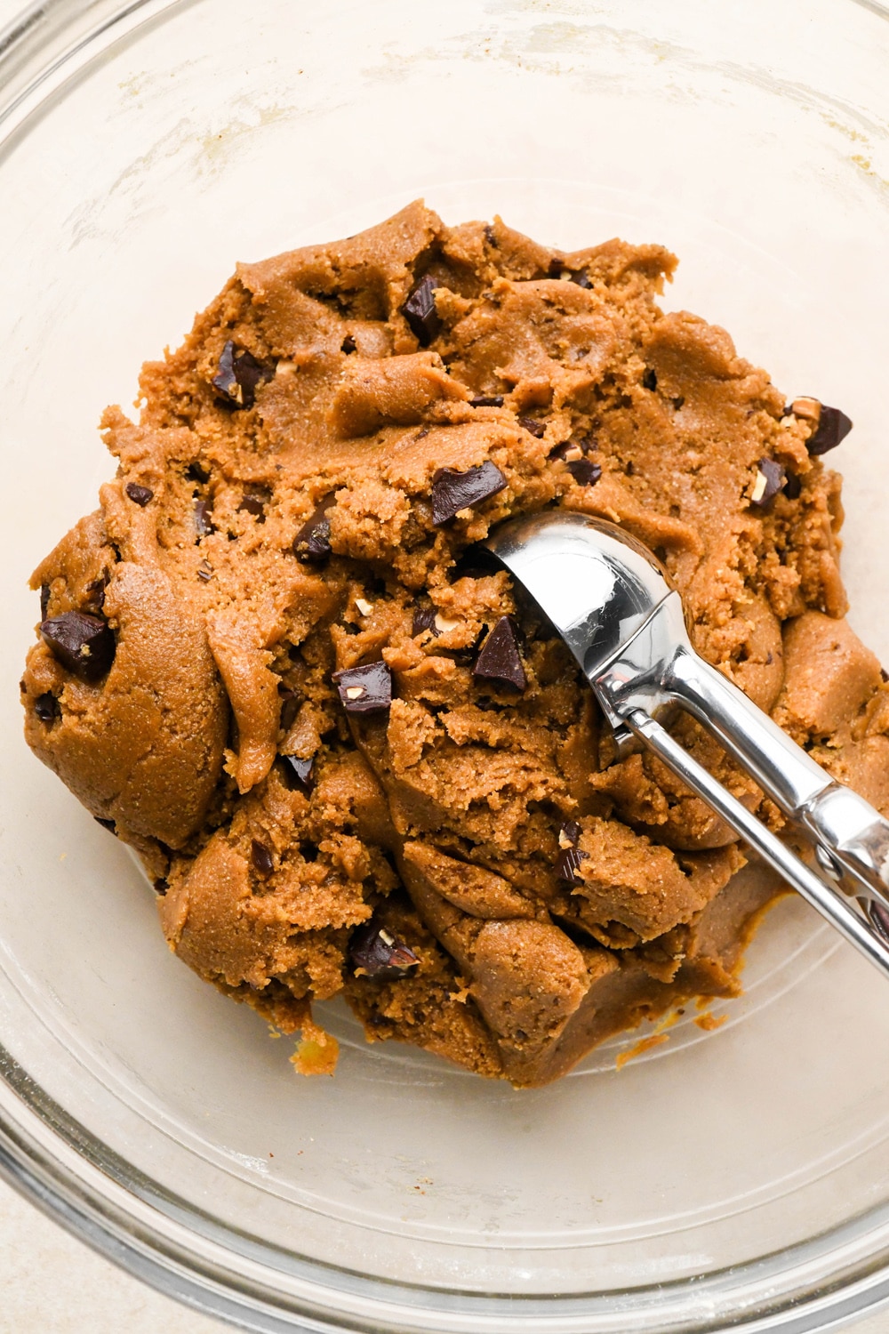 How to make Dark Chocolate Espresso Chickpea Flour Cookies: A cookie scoop scooping cookie dough out of glass bowl full of cookie dough.