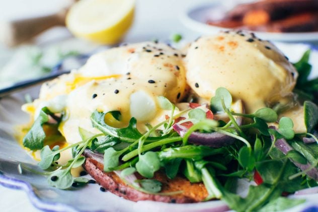 Paleo mediterranean eggs benedict made with layers of spiced sweet potato planks, a bright + tangled lemony salad of arugula, cherry tomatoes, cucumber and red onion, perfectly poached eggs and a paprika spiked tahini hollandaise sauce.