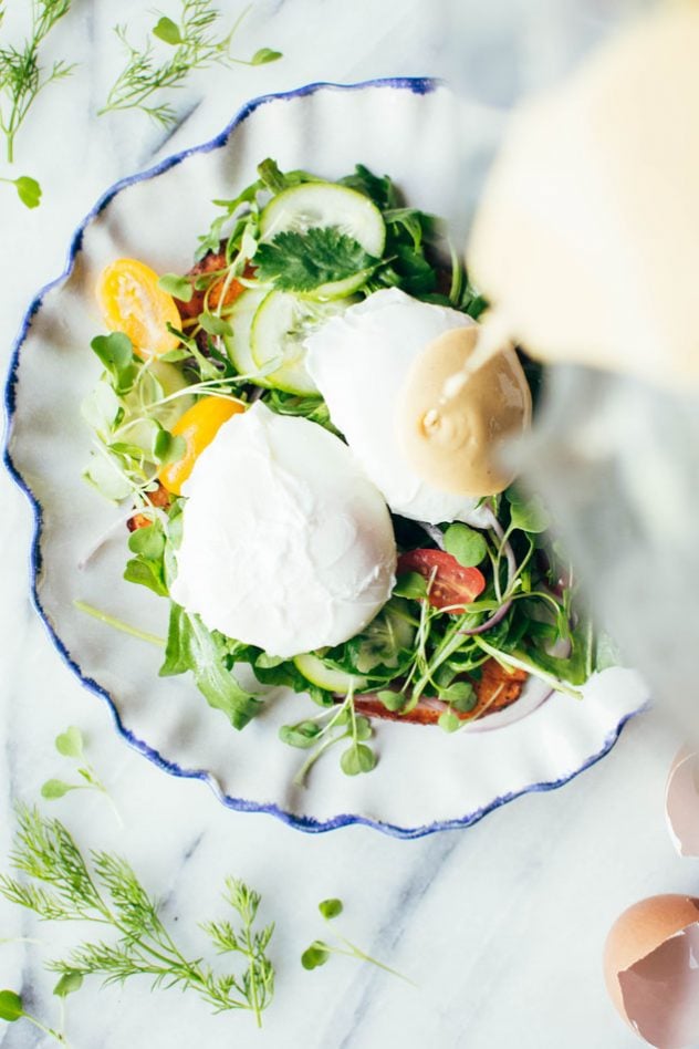 Paleo mediterranean eggs benedict made with layers of spiced sweet potato planks, a bright + tangled lemony salad of arugula, cherry tomatoes, cucumber and red onion, perfectly poached eggs and a paprika spiked tahini hollandaise sauce.