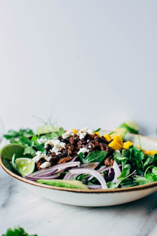 Mango chorizo taco salad bowls with green sauce! Spicy crumbled chorizo layered over salad greens with a rainbow of veggies and all your favorite toppings.