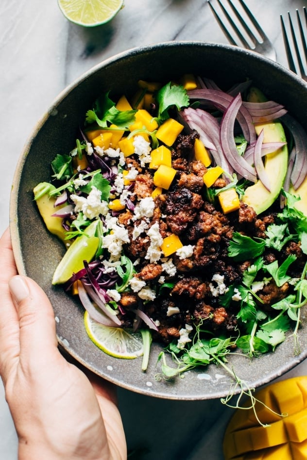 Mango chorizo taco salad bowls with green sauce! Spicy crumbled chorizo layered over salad greens with a rainbow of veggies and all your favorite toppings.