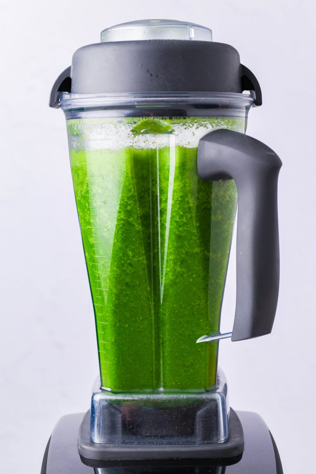 Straight on shot of a bright green blended green juice in a Vitamix blender. In front of a white background.