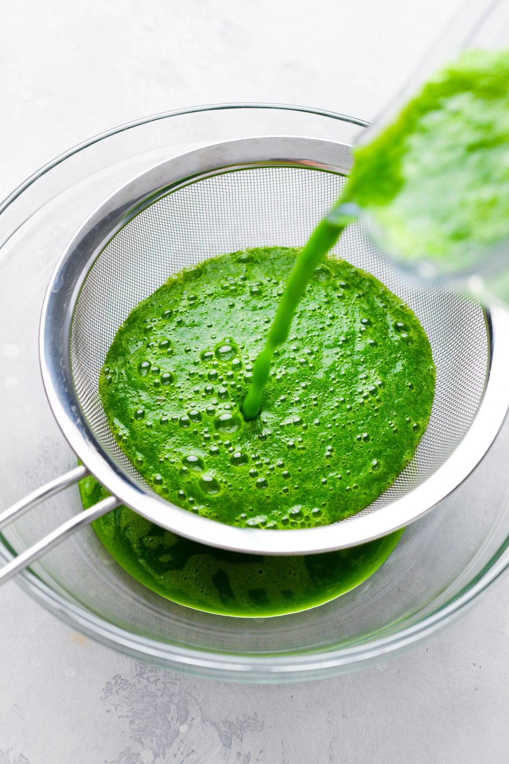 Image of pouring blended green juice into a strainer positioned over a large bowl to strain out the solids.