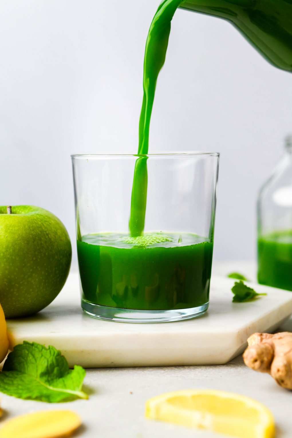 Straight on shot of pouring green juice in a small glass - on a white background.
