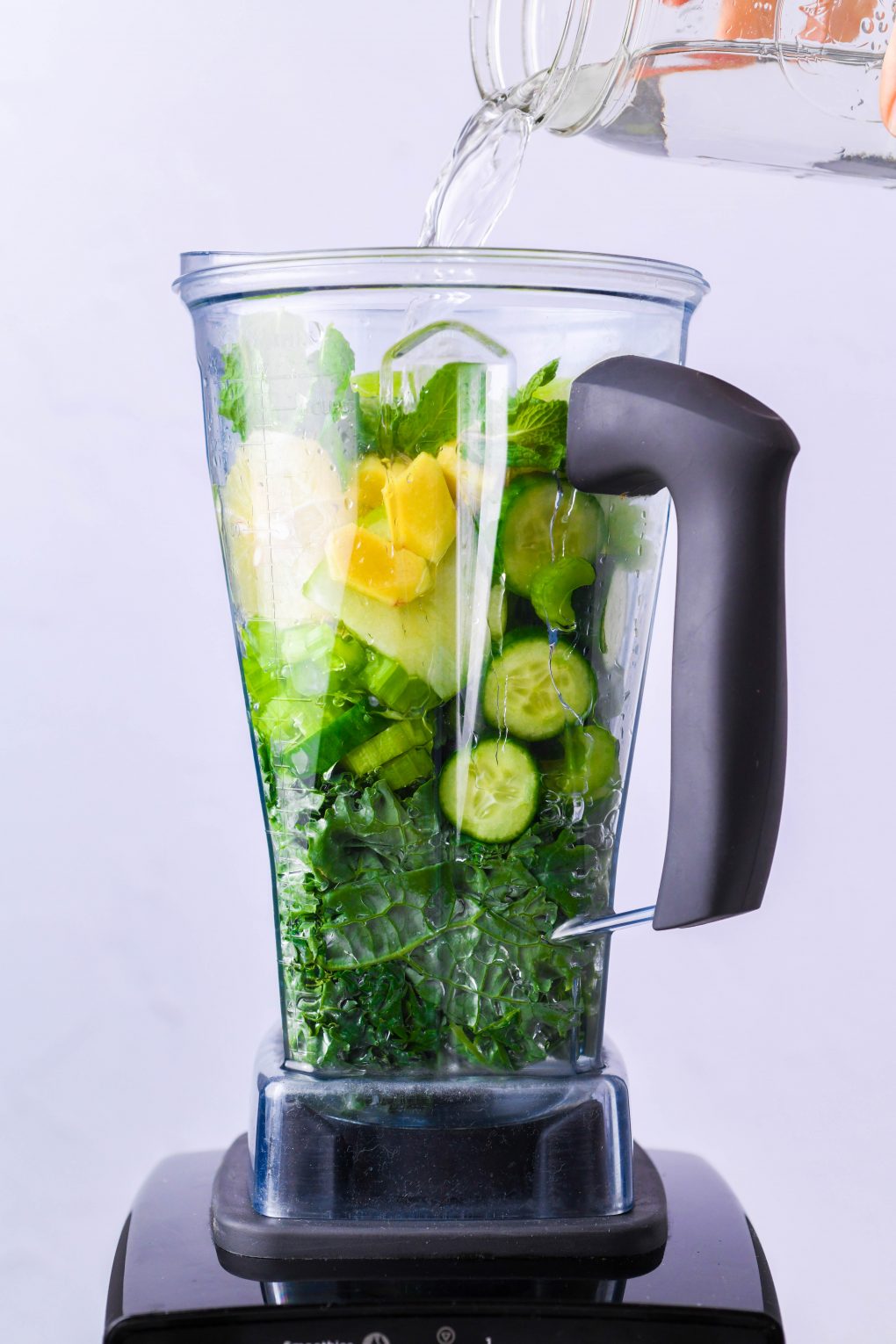 Straight on shot of a blender container filled with all the ingredients for green juice