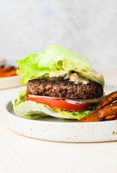 Straight on shot of a bunless lettuce wrap burger on a ceramic plate, next to sweet potato fries
