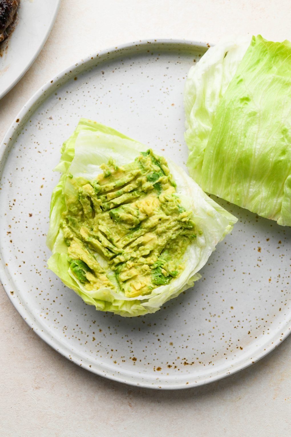 How to make a bunless lettuce wrap burger: lettuce wedges on a plate topped with smashed avocado.