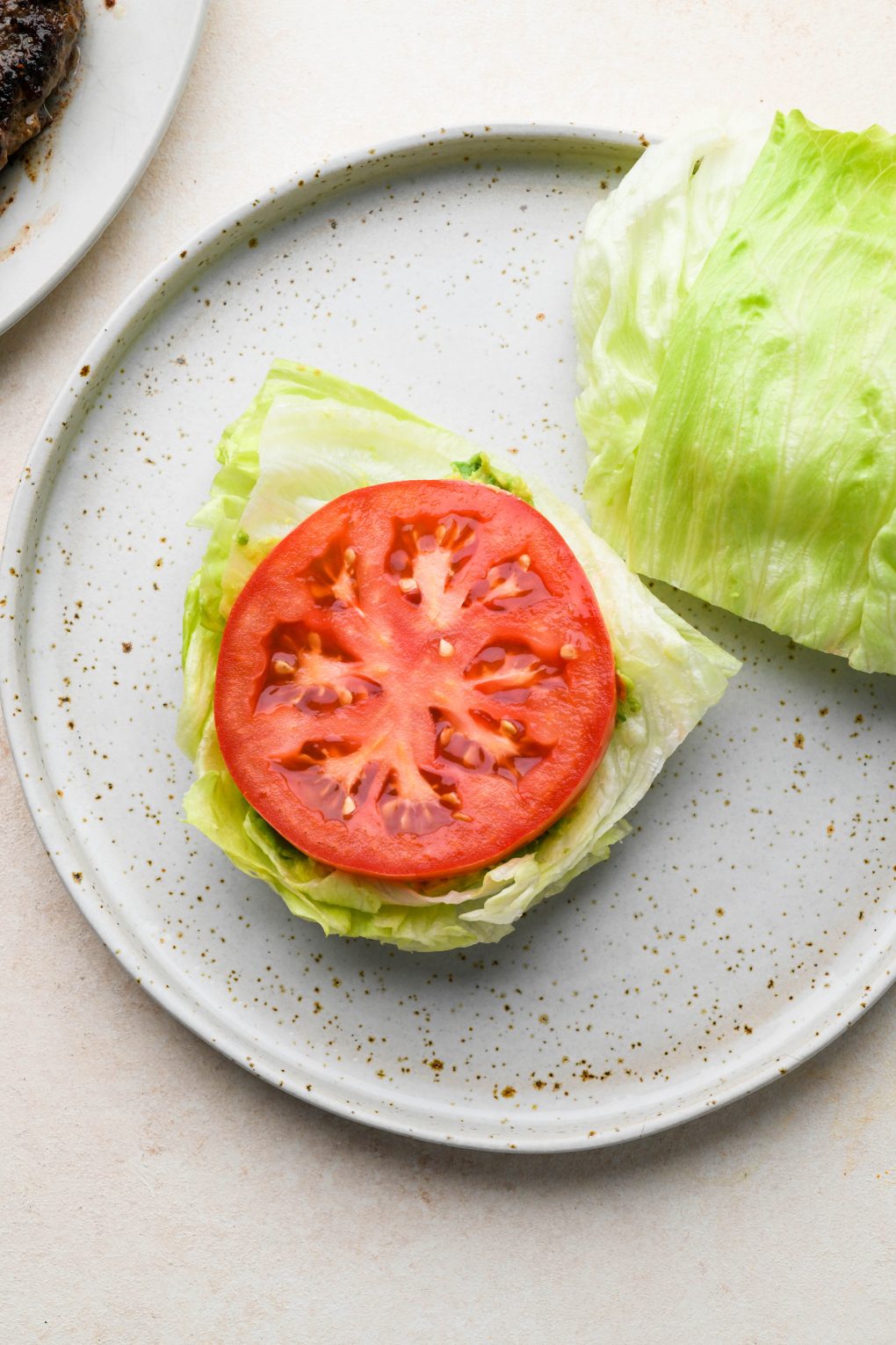 How to make a bunless lettuce wrap burger: lettuce wedges on a plate topped with smashed avocado and tomato.