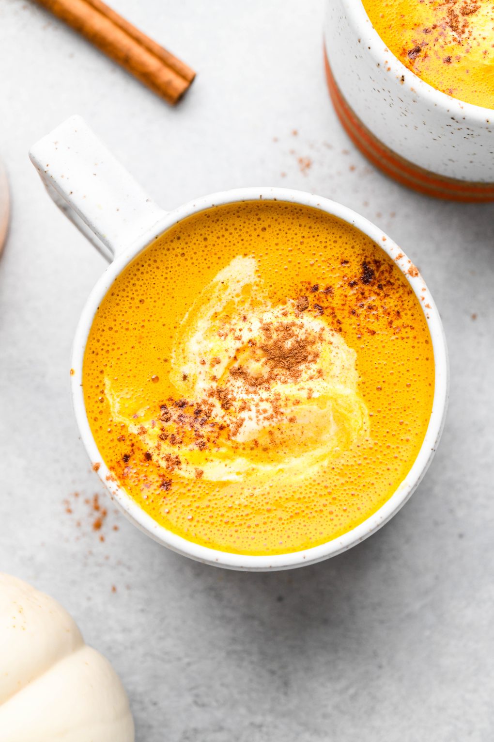 Golden orange hued creamy pumpkin spice bulletproof latte. In a speckled mug sprinkled with cinnamon.