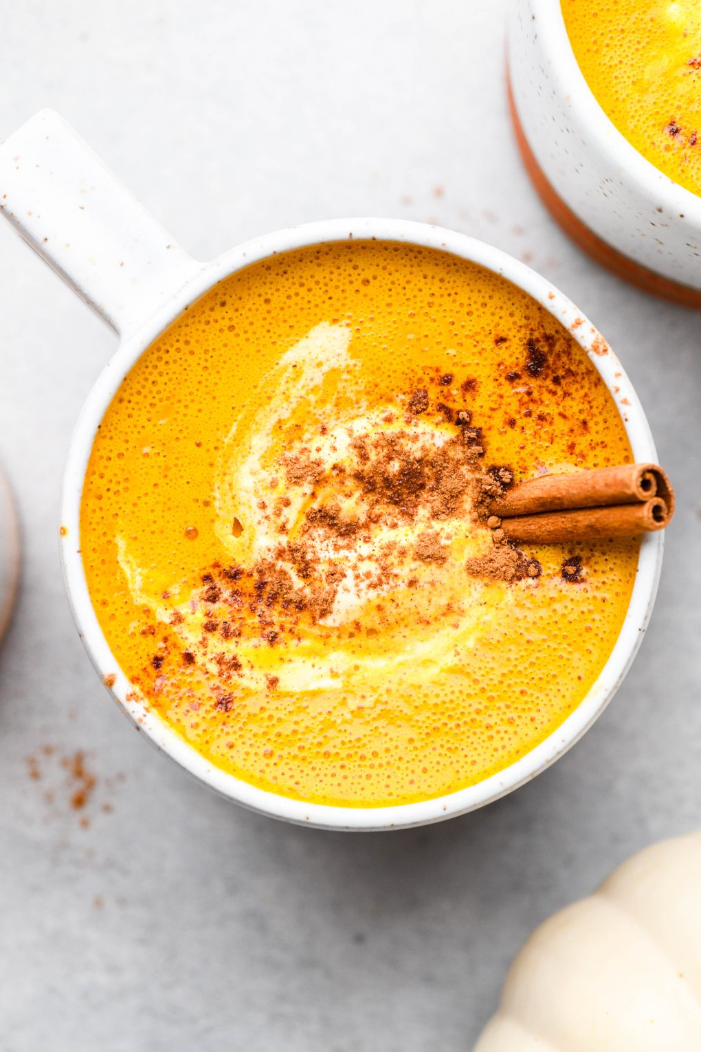Golden orange hued creamy pumpkin spice bulletproof latte. In a speckled mug sprinkled with cinnamon.
