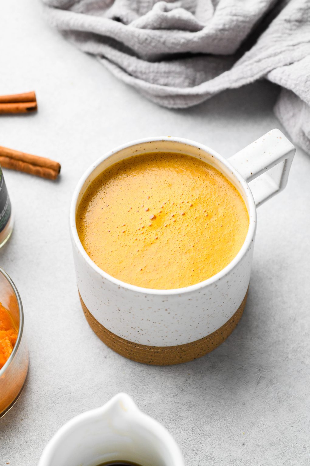 Golden orange hued creamy pumpkin spice bulletproof latte. In a speckled mug.