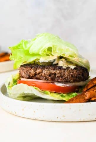 Straight on shot of a bunless lettuce wrap burger on a ceramic plate, next to sweet potato fries