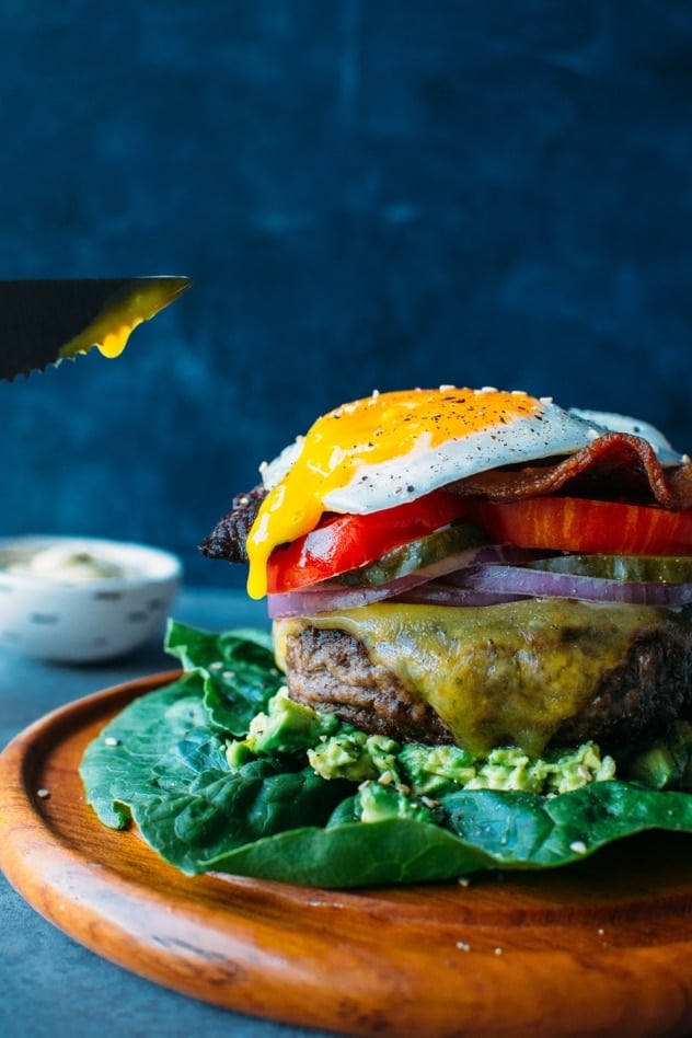 A knife cutting into the egg yolk on top of a bunless burger.