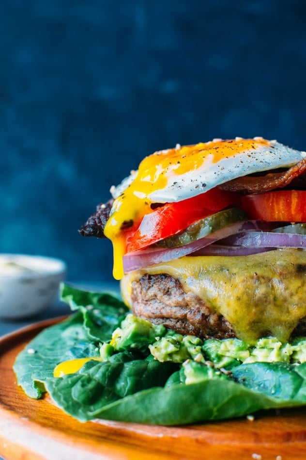 Bunless burger with toppings on a plate with egg yolk dripping down the side of the burger from sunny side up egg.