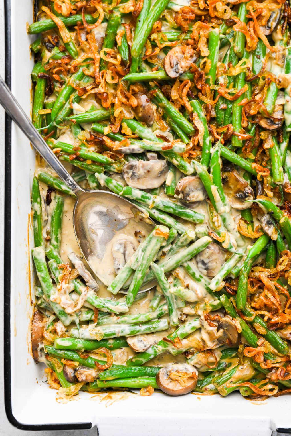 Baked gluten free green bean casserole topped with crispy shallots, with a scoop taken out to expose the creamy interior.