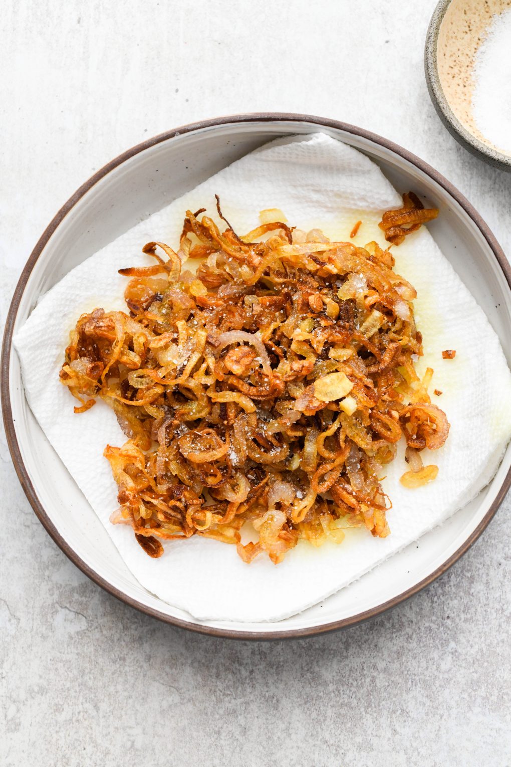 Crispy fried shallots on a paper towel in a small dish topped with salt.