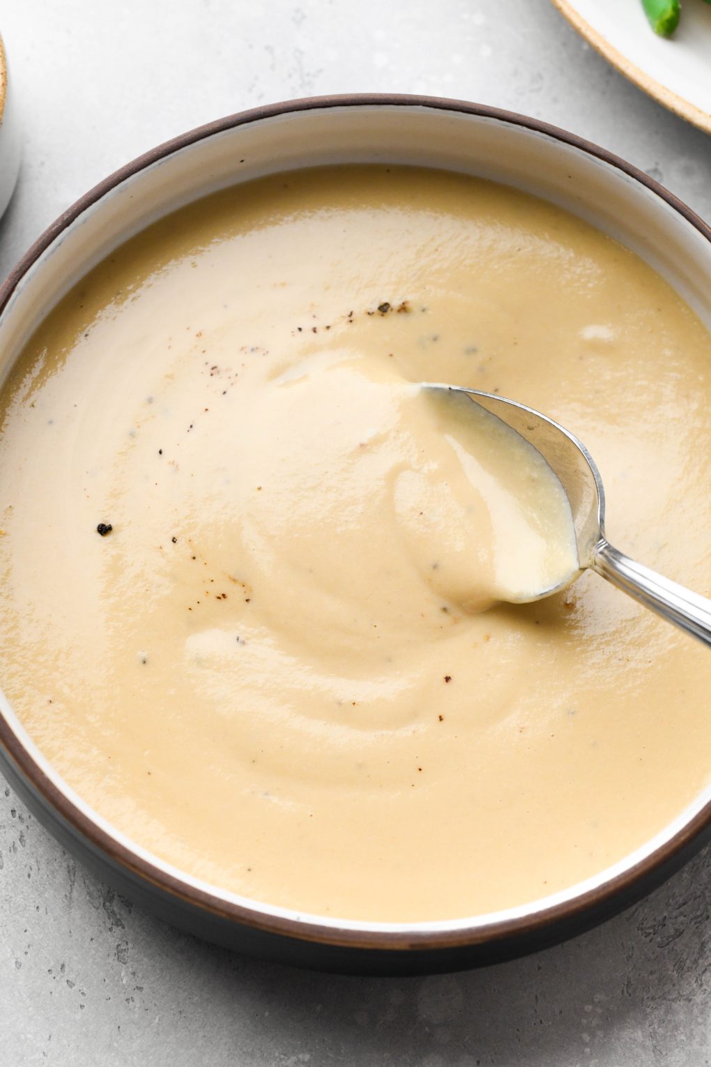 Close up image of a small bowl of make ahead whole30 gravy with a spoon dipping into it.