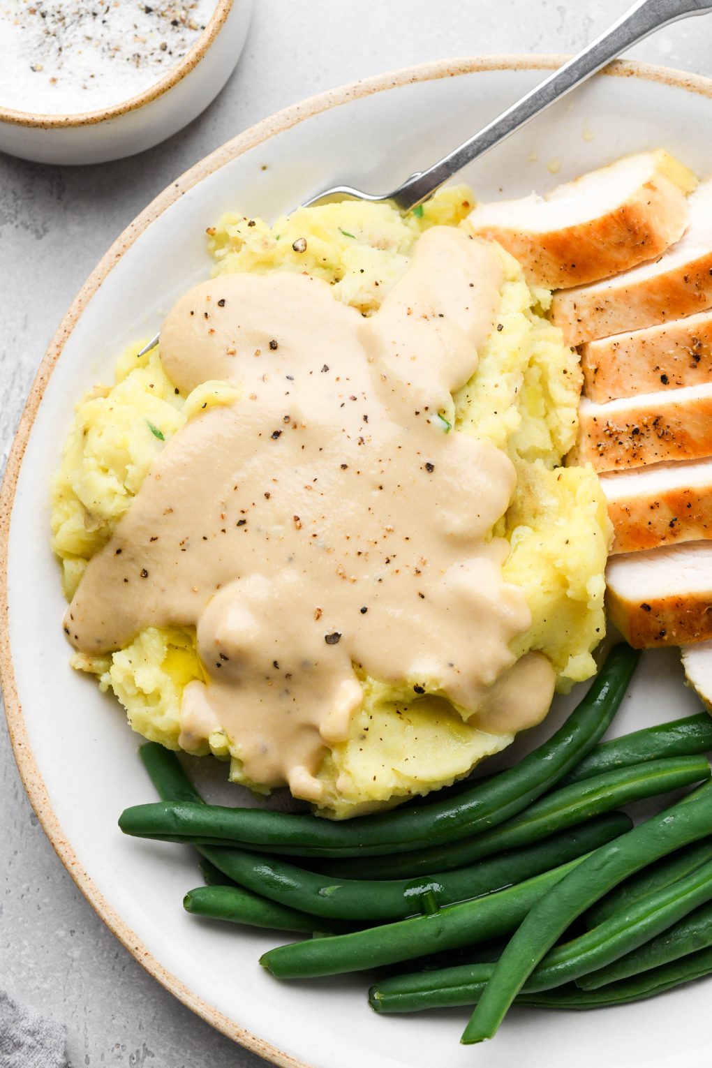 Mashed potatoes with Whole30 gravy, green beans, and thinly sliced turkey on a plate. 