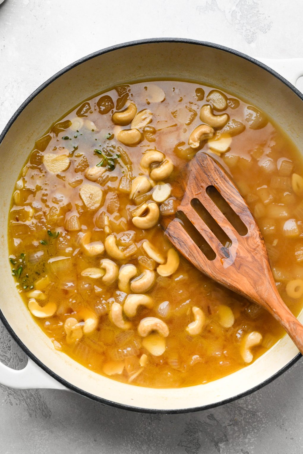 Photos showing how to make Whole30 gravy - broth reduced in skillet with diced onions, raw cashews, and fresh thyme.