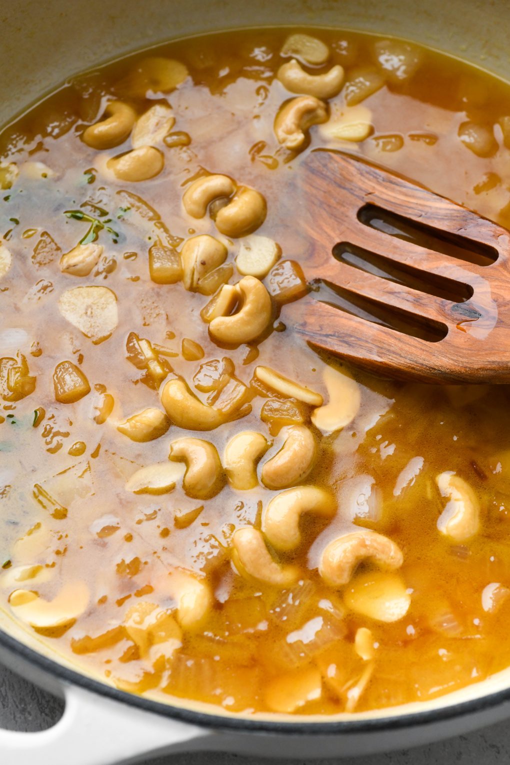 Photos showing how to make Whole30 gravy - close up image of broth reduced in skillet with diced onions, raw cashews, and fresh thyme.