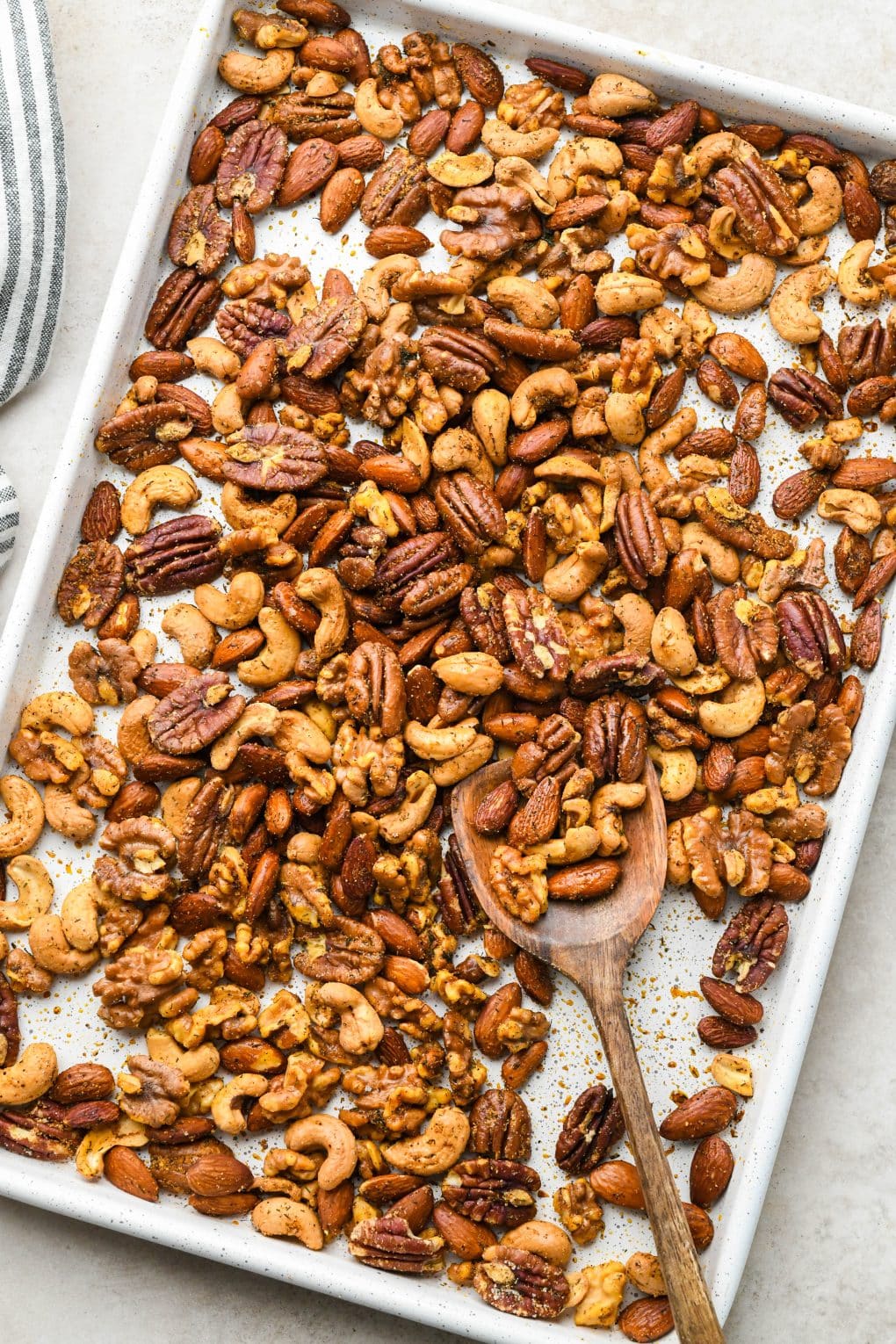 A white speckled baking sheet filled with roasted spiced nuts.