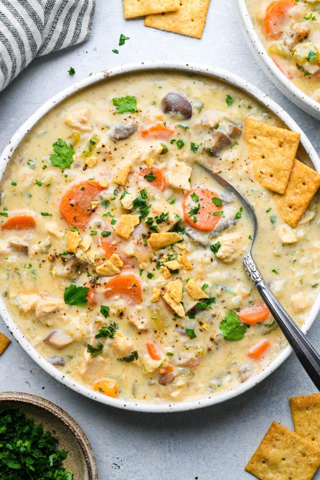 A wide shallow speckled bowl of creamy dairy free chicken and cauliflower rice soup, topped with fresh herbs and gluten free crackers.