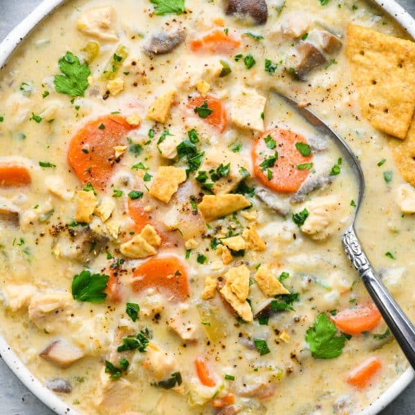 Overhead image of a large shallow bowl of creamy dairy free chicken and cauliflower rice soup filled with chunks of carrot, celery, onions, mushrooms, and chicken.