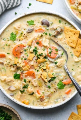 A wide shallow speckled bowl of creamy dairy free chicken and cauliflower rice soup, topped with fresh herbs and gluten free crackers.