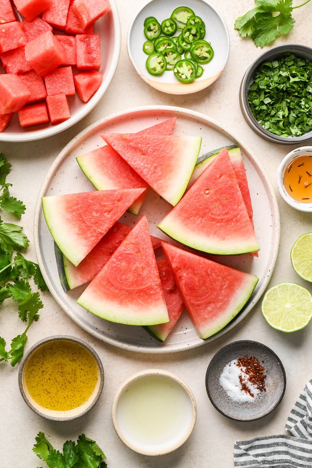 Ingredients for spicy watermelon salad on various ceramics, on a light cream colored background.