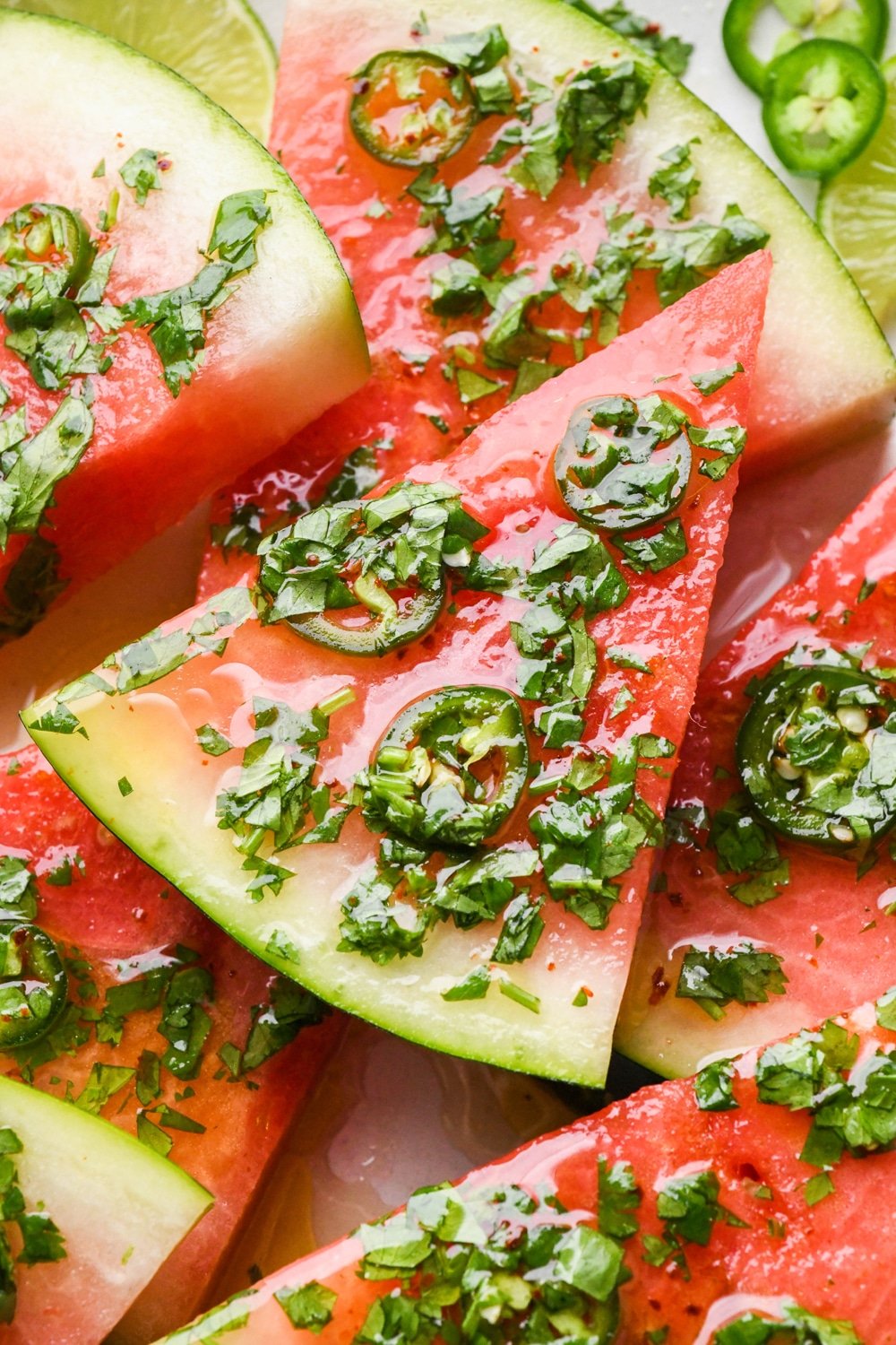 Watermelon slices piled on top of each other on a serving platter and topped with cilantro lime vinaigrette.