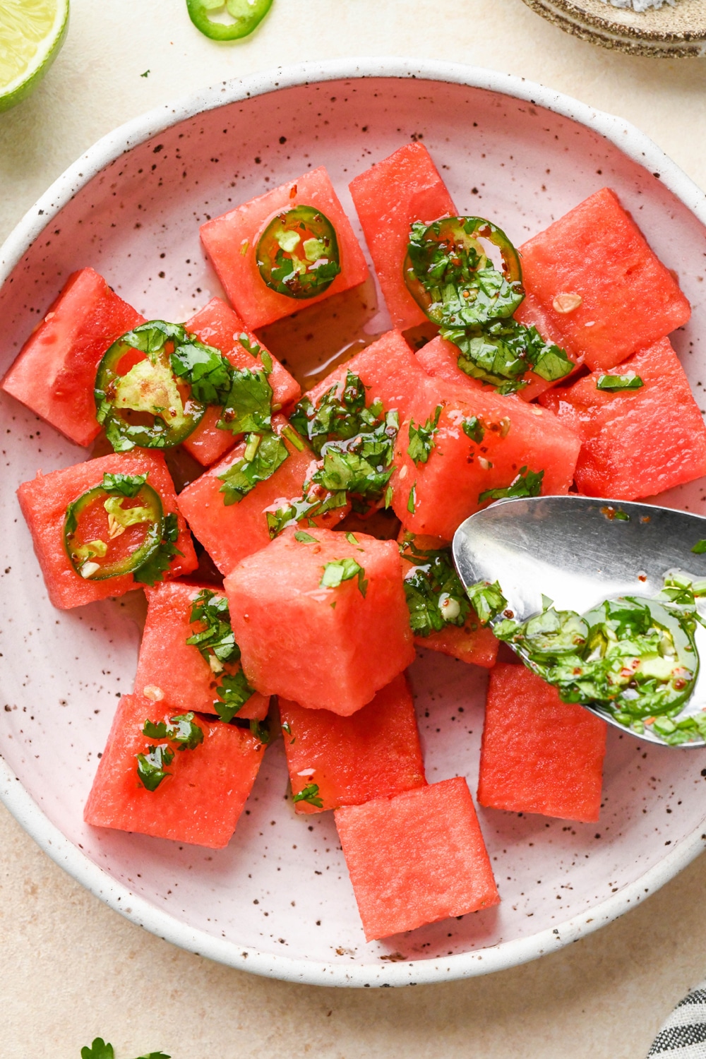 How to make spicy watermelon salad: Spooning the dressing over cubed watermelon in a shallow bowl. 