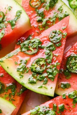 Watermelon slices piled on top of each other on a serving platter and topped with cilantro lime vinaigrette.