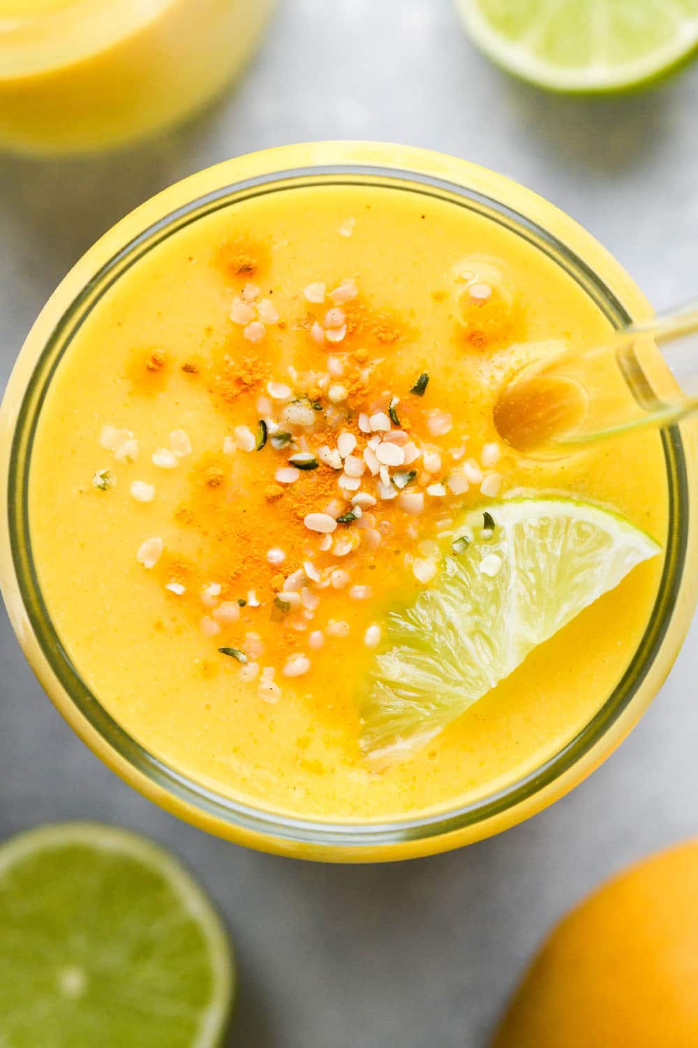 Overhead image of a cup of mango turmeric smoothie garnished with dried turmeric, hemp seeds, and a lime wedge.