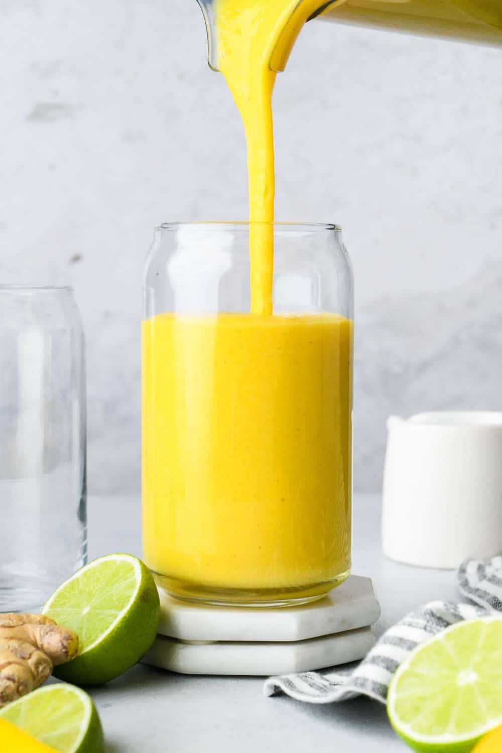 How to make a Mango Ginger Turmeric Smoothie: Pouring blended mango smoothie into a glass cup.