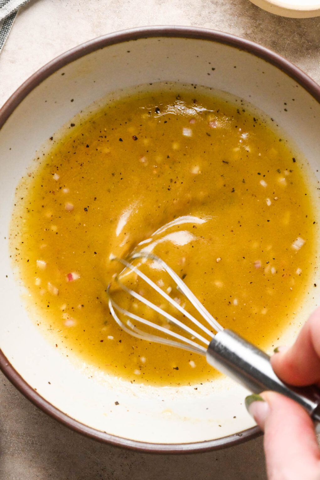How to make Asian Pear and Walnut Salad with Maple Mustard Dressing: A hand with a whisk whisking together the dressing in a medium-sized ceramic bowl.