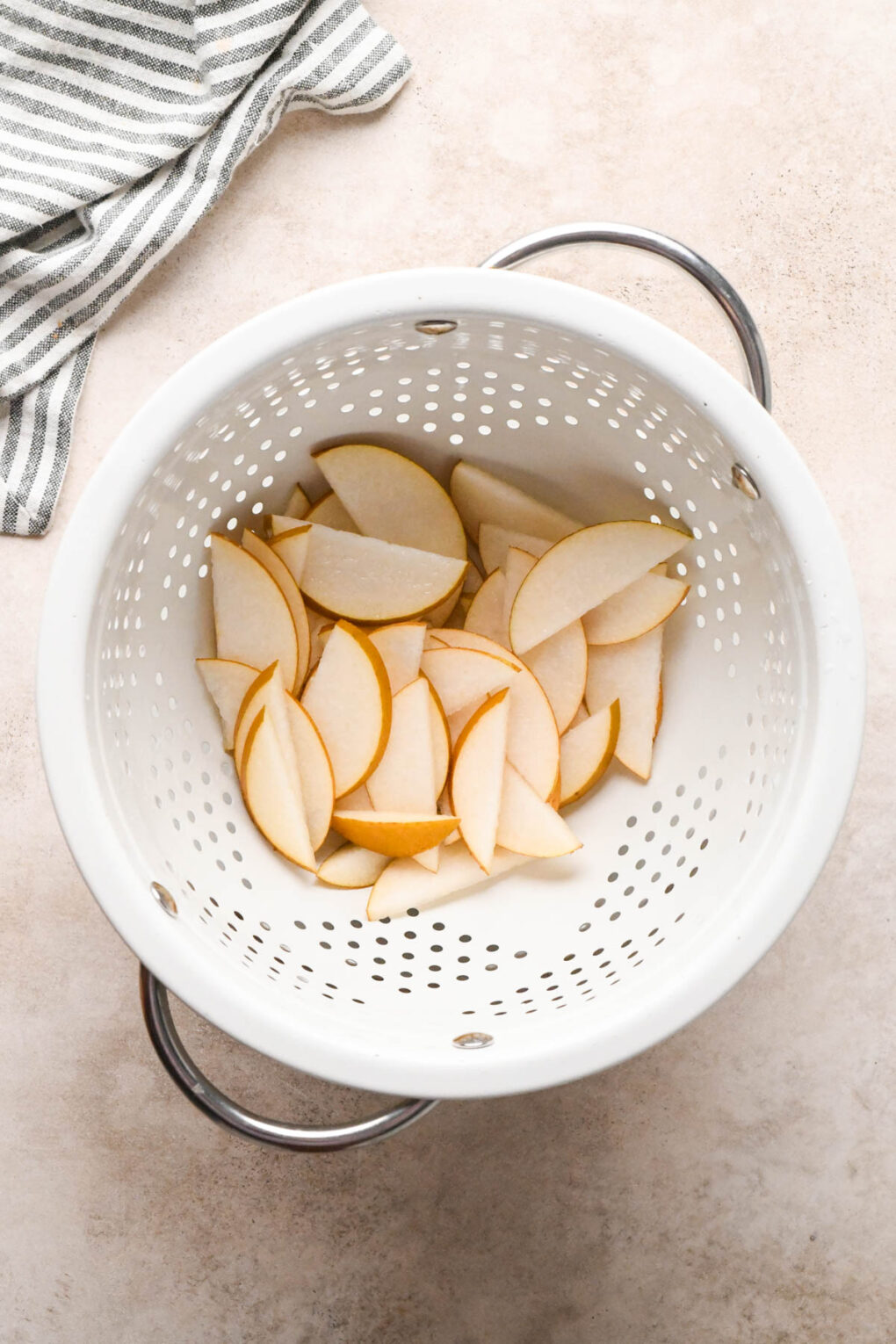 How to make Asian Pear and Walnut Salad with Maple Mustard Dressing: Sliced Asian pears in a white colander, drained from the bowl of lemon water.